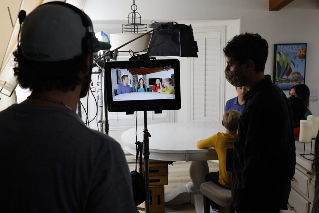 Camera operator filming two people beside a window during a video production.